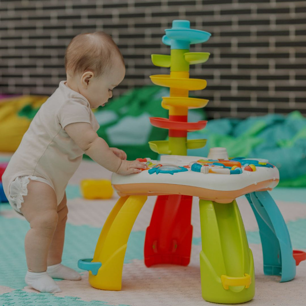 Baby playing with a colorful toy table and stacking tower in a playroom.