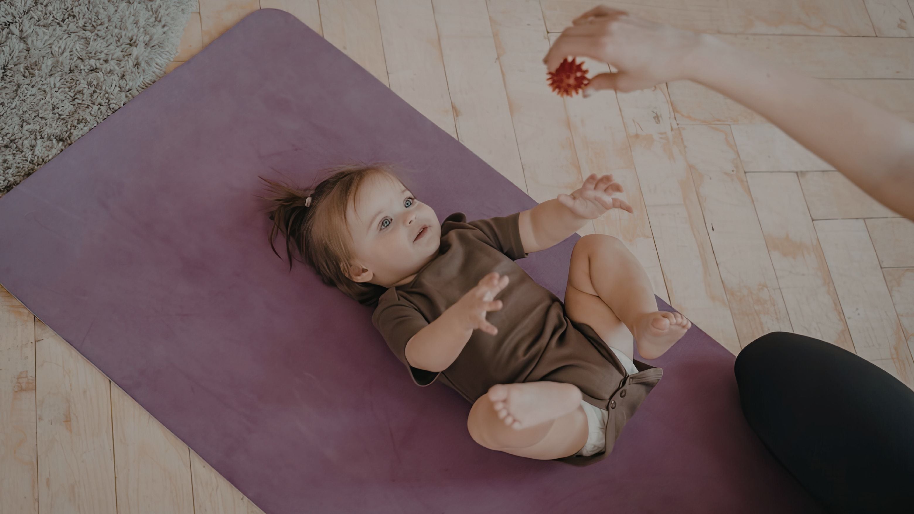 Child lying on a yoga mat with an adult's hand reaching out