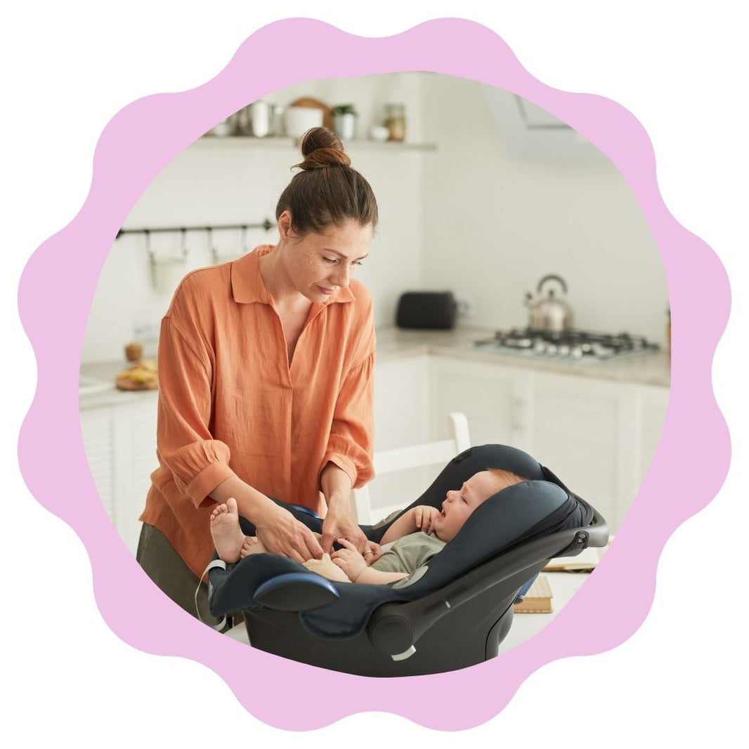 Woman adjusting a baby in a car seat in a kitchen.